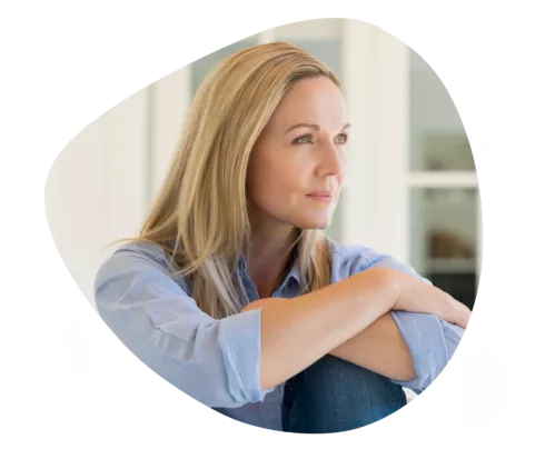 Eine Frau hält ihre angewinkelten Knie und schaut nachdenklich in die Ferne.