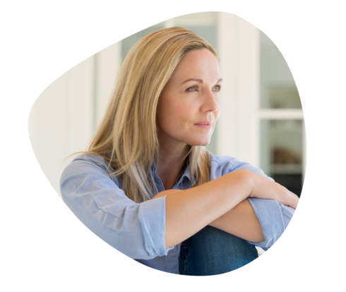 Eine Frau hält ihre angewinkelten Knie und schaut nachdenklich in die Ferne.