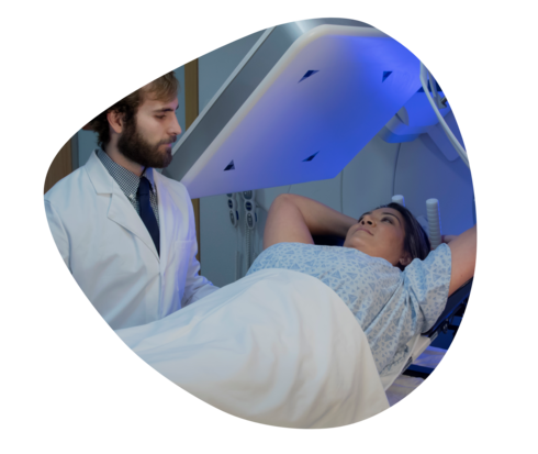 Metastasierter Brustkrebs: Strahlentherapie Eine Frau liegt unter einem Bestrahlungsgerät. Ein Mann im weißen Kittel schaut zu.