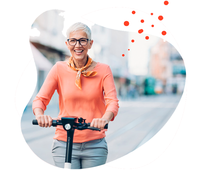 Leben mit Brustkrebs: Eine grauhaarige Frau fährt lachend mit einem Elektroroller