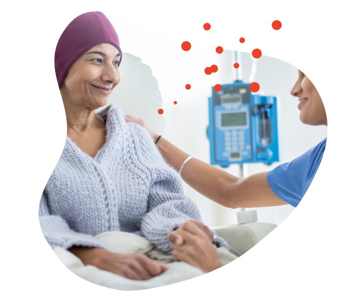 Metastasierender Brustkrebs: Chemotherapie Eine Frau bekommt auf einem Behandlungsstuhl eitzend eine Injektion. Eine andere Frau hält ihre Hand und streicht ihr mit der anderen über den Oberamr