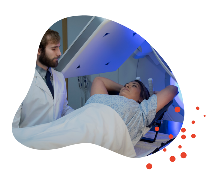 Metastasierender Brustkrebs: Strahlentherapie Eine Frau liegt unter einem Bestrahlungsgerät. Ein Mann im weißen Kittel schaut zu.