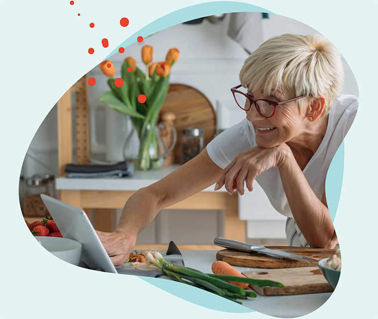 Leben mit Brustkrebs: Eine grauhaarige Frau steht in der Küche und schaut ein Rezept auf einem Tablet nach