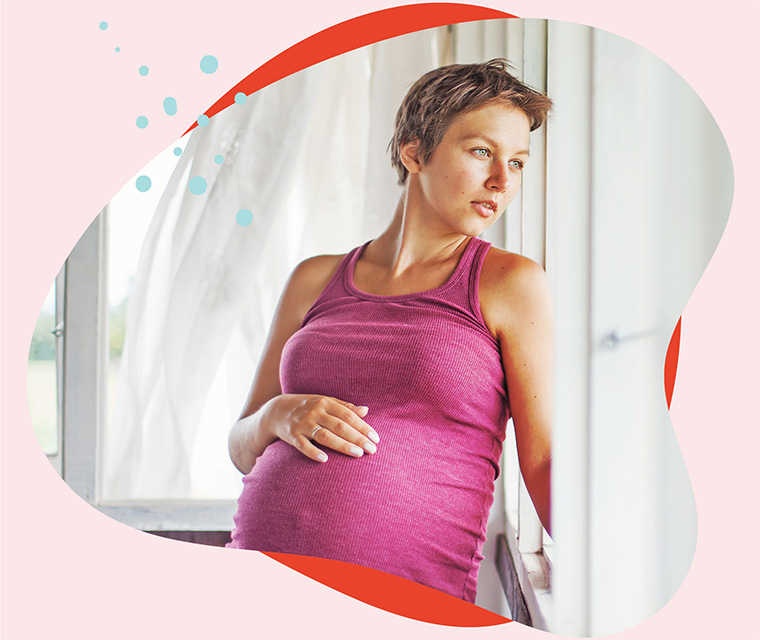 Leben mit Brustkrebs: Eine schwangere Frau streicht sich über den Bauch und schaut aus dem Fenster