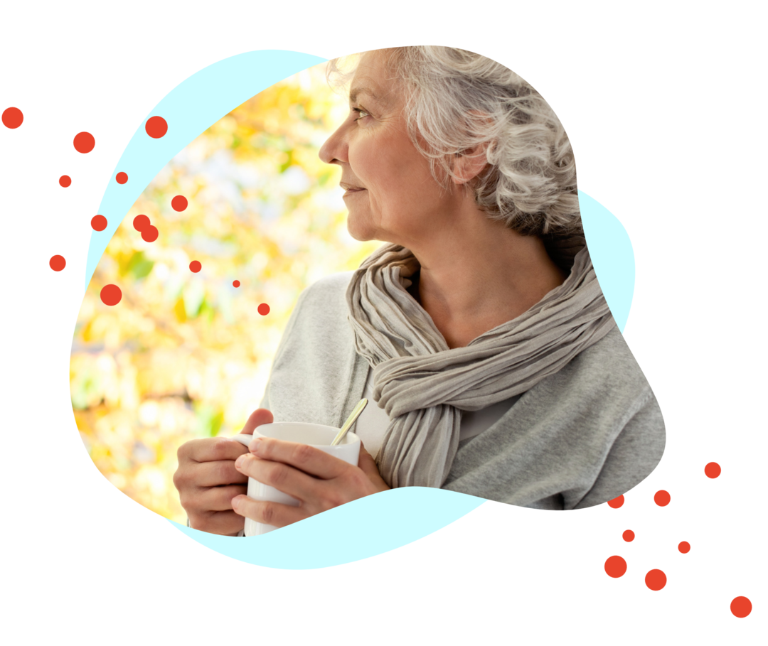 Eine Frau mit einer Tasse in den Händen schaut nachdenklich zur Seite.