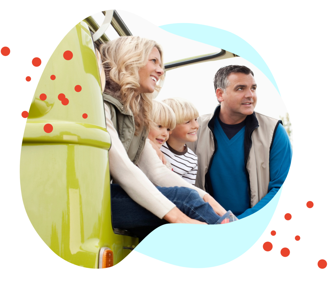 Eine Frau, zwei Kinder und ein Mann schauen aus der hochgeklappten Heckklappe eins VW Busses.