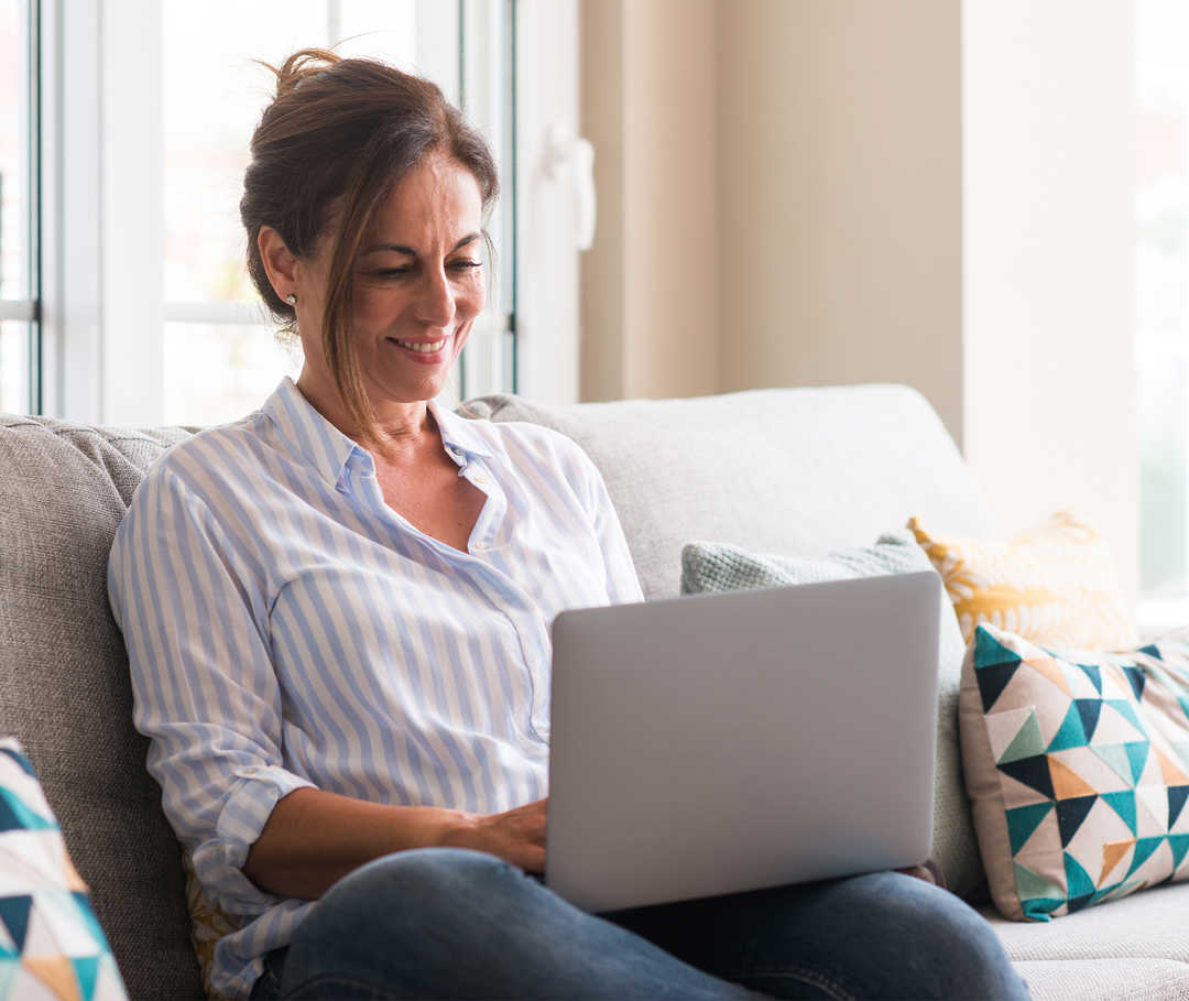 Eine Frau sitzt auf einem Sofa und schaut auf ihr Notebook auf ihrem Schoß.