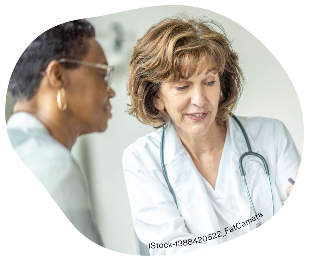 Eine Frau im weißen Kittel deutet auf ein Klemmbrett, neben ihr steht eine weitere Frau.